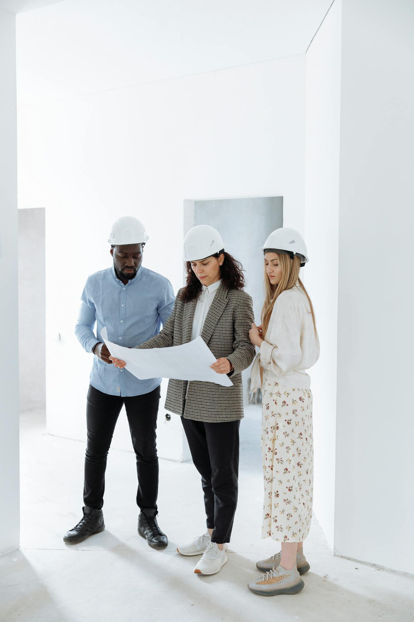 Three people in hard hats examining construction plans in a new home's interior.